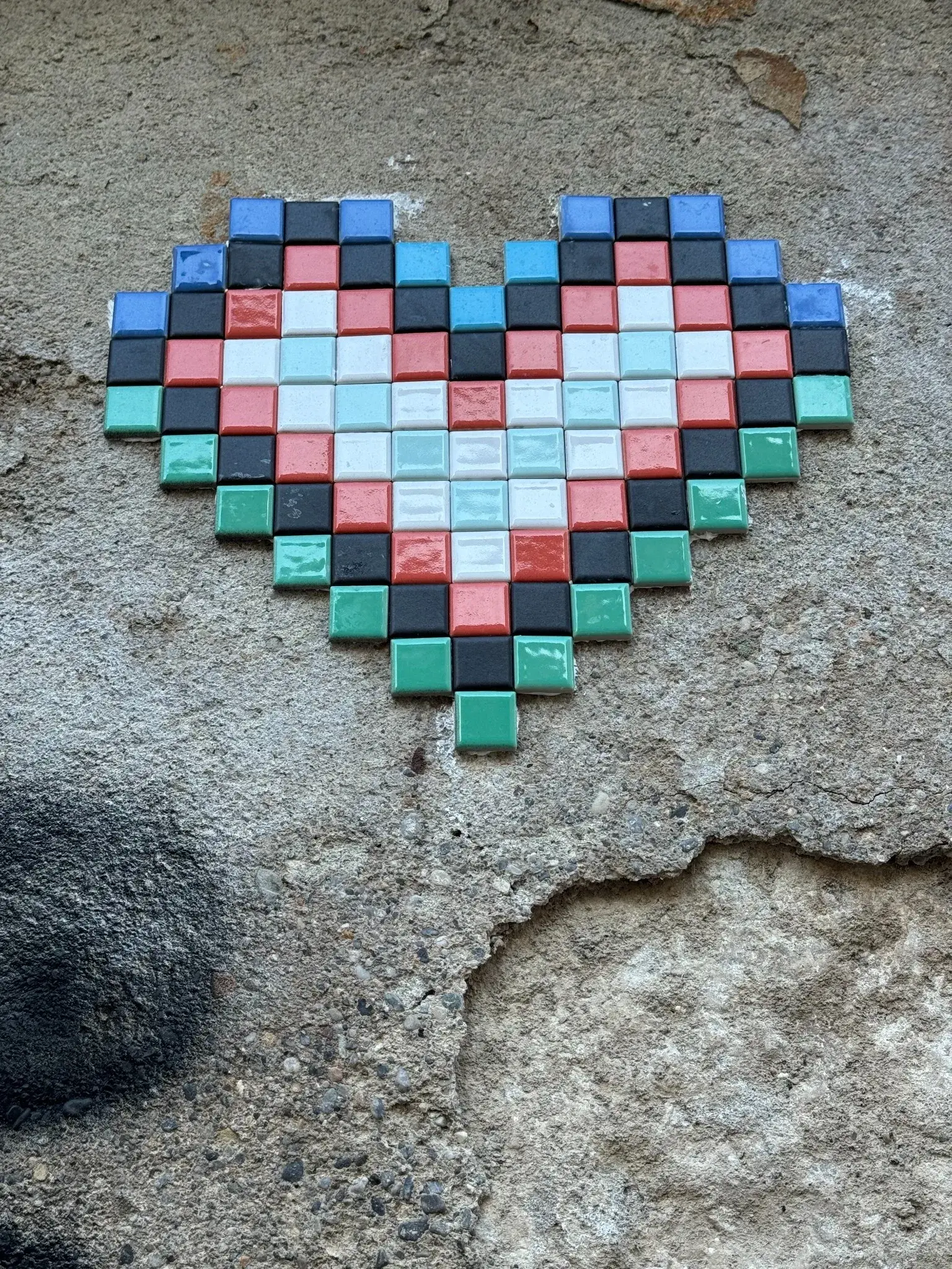 Cuore composto da tessere colorate simili a pixel su una parete urbana dall’intonaco consumato