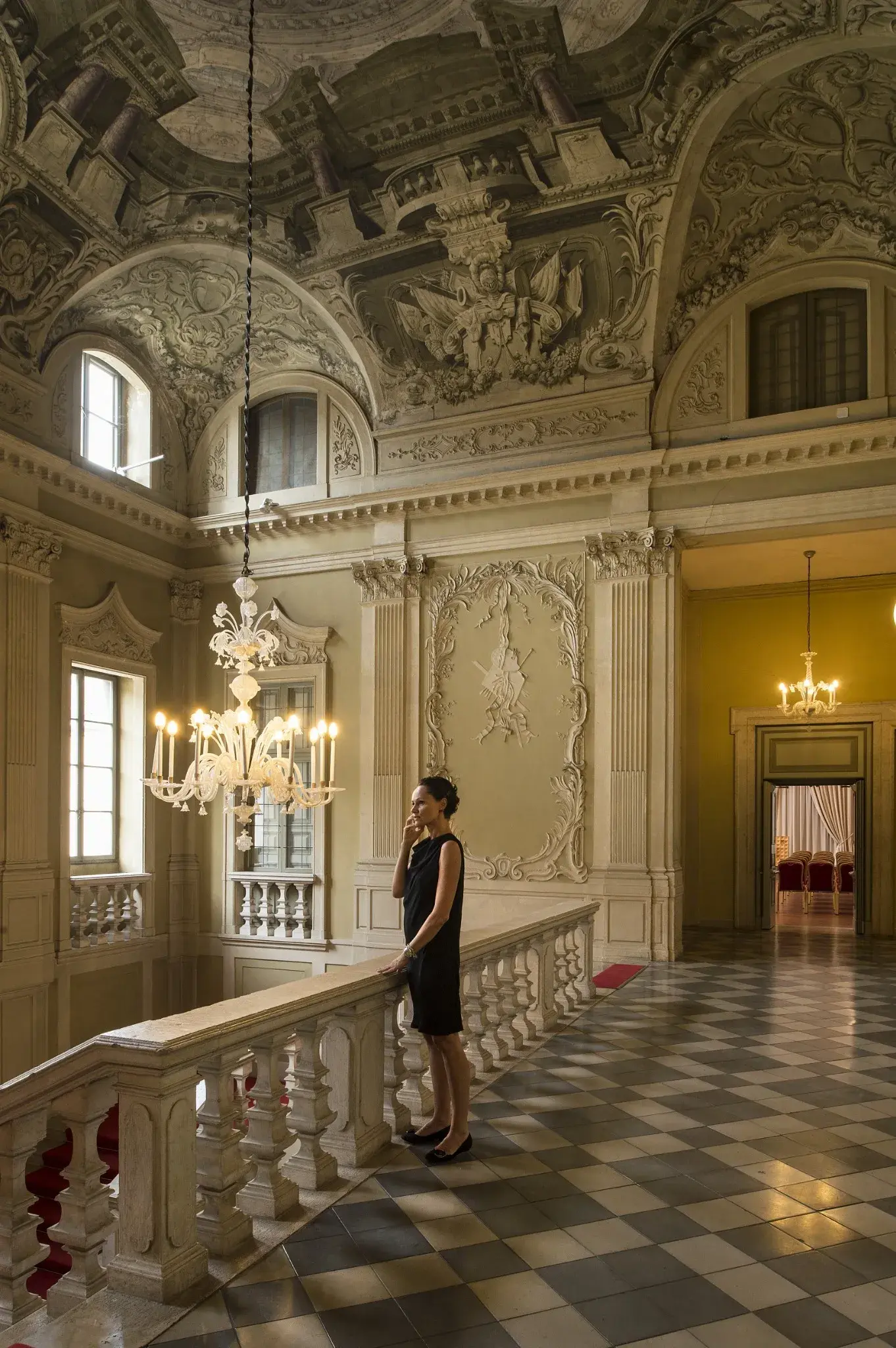 Donna presso la balaustra dello scalone di Palazzo Santangelo a Brescia, tra lampadari e decorazioni storiche